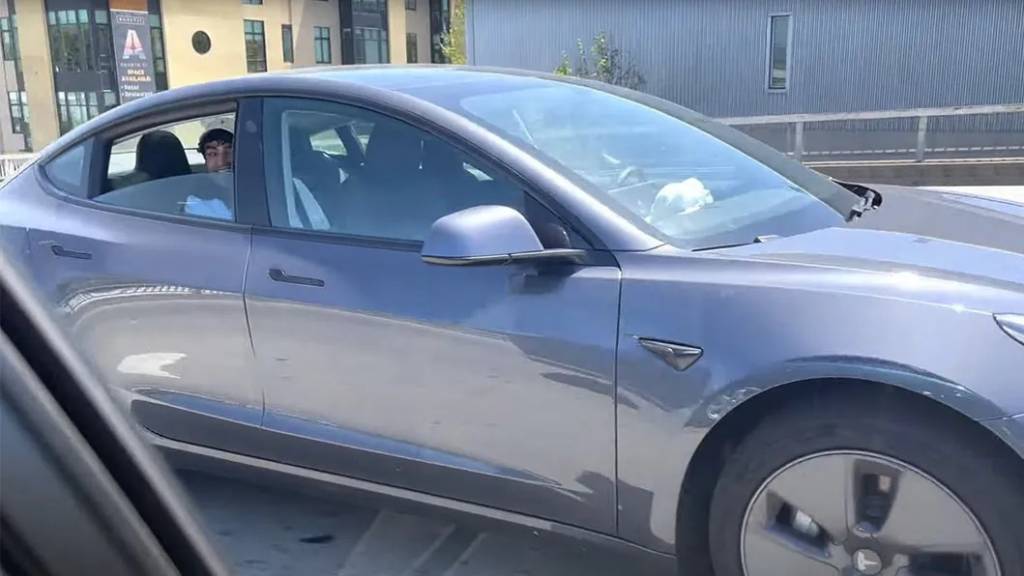 Tesla-Model-3-Autopilot – banco de trás Tesla Model 3 cinza visto de lado com jovem no banco de trás